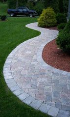 Curved stone garden path bordered by green lawn and shrubs, with a parked car in the background