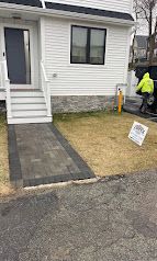 Front yard walkway with pavers, small lawn, and a person in a neon jacket near a white house