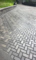 Gray herringbone brick driveway beside a grassy border and stone wall