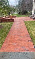 Brick walkway leading through a yard toward a house, bordered by grass and low brick planters