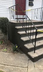 Concrete steps with black metal railing leading to a red door on a white house.