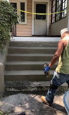 Worker power-washing concrete steps beside a house entrance with yellow caution tape across the porch