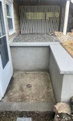 Empty concrete stairwell opening leading to a basement with a gravel-covered area beyond.