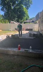Person standing in a backyard excavation, with concrete foundation walls and construction materials nearby