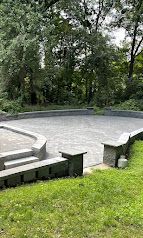 Empty circular stone amphitheater in a wooded park with grassy foreground