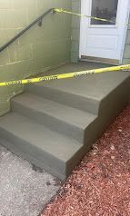 Concrete front steps blocked with yellow caution tape beside a white door.