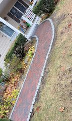Curved brick walkway bordered by white edging beside a house and garden shrubs