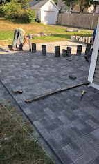 Patio under construction with gray pavers, scattered blocks, and tools in a backyard.