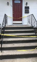 House front steps blocked by yellow caution tape leading to a red door