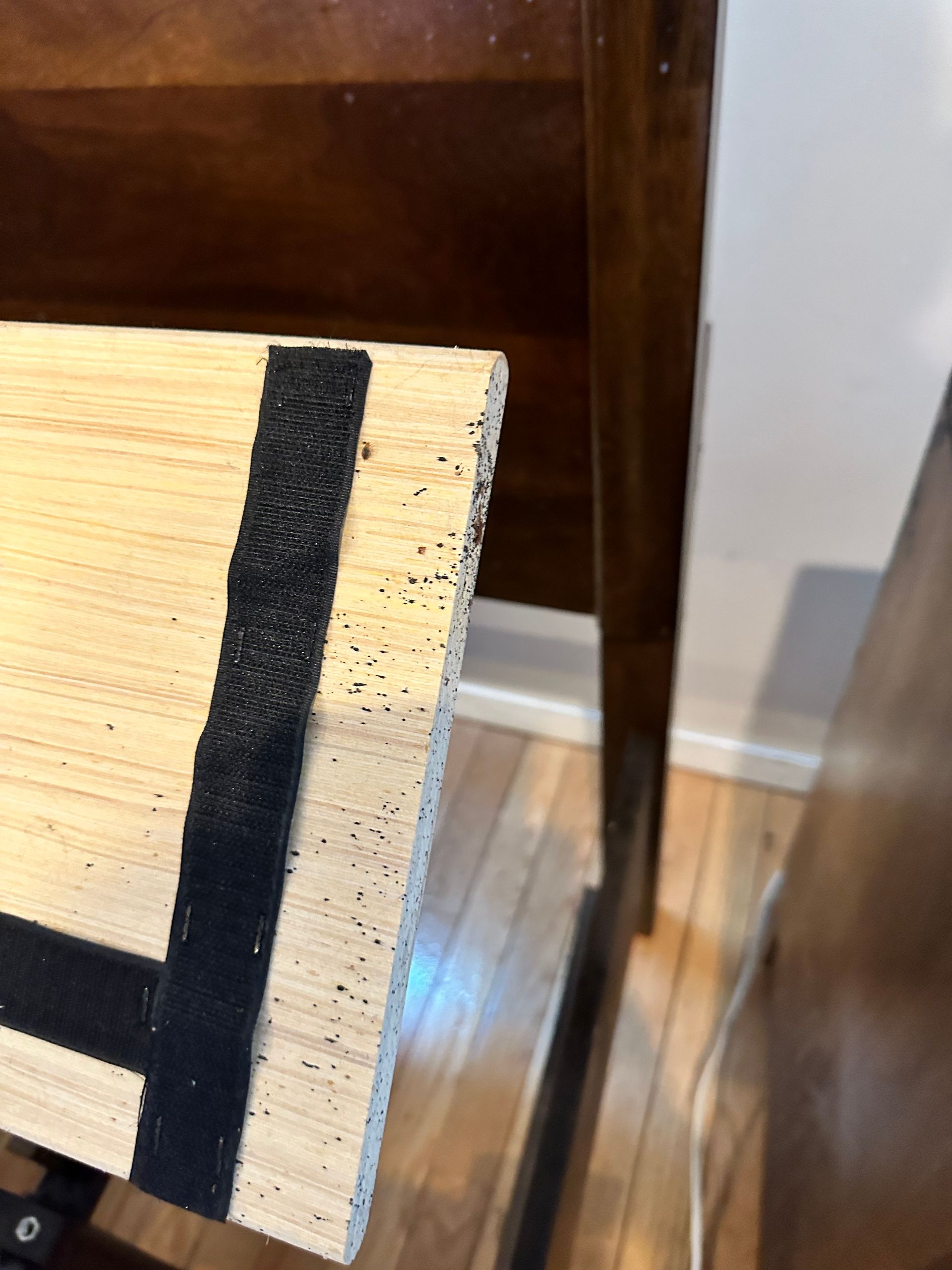 Close-up of a wooden edge with a black painted stripe beside a brown cabinet and wood floor.