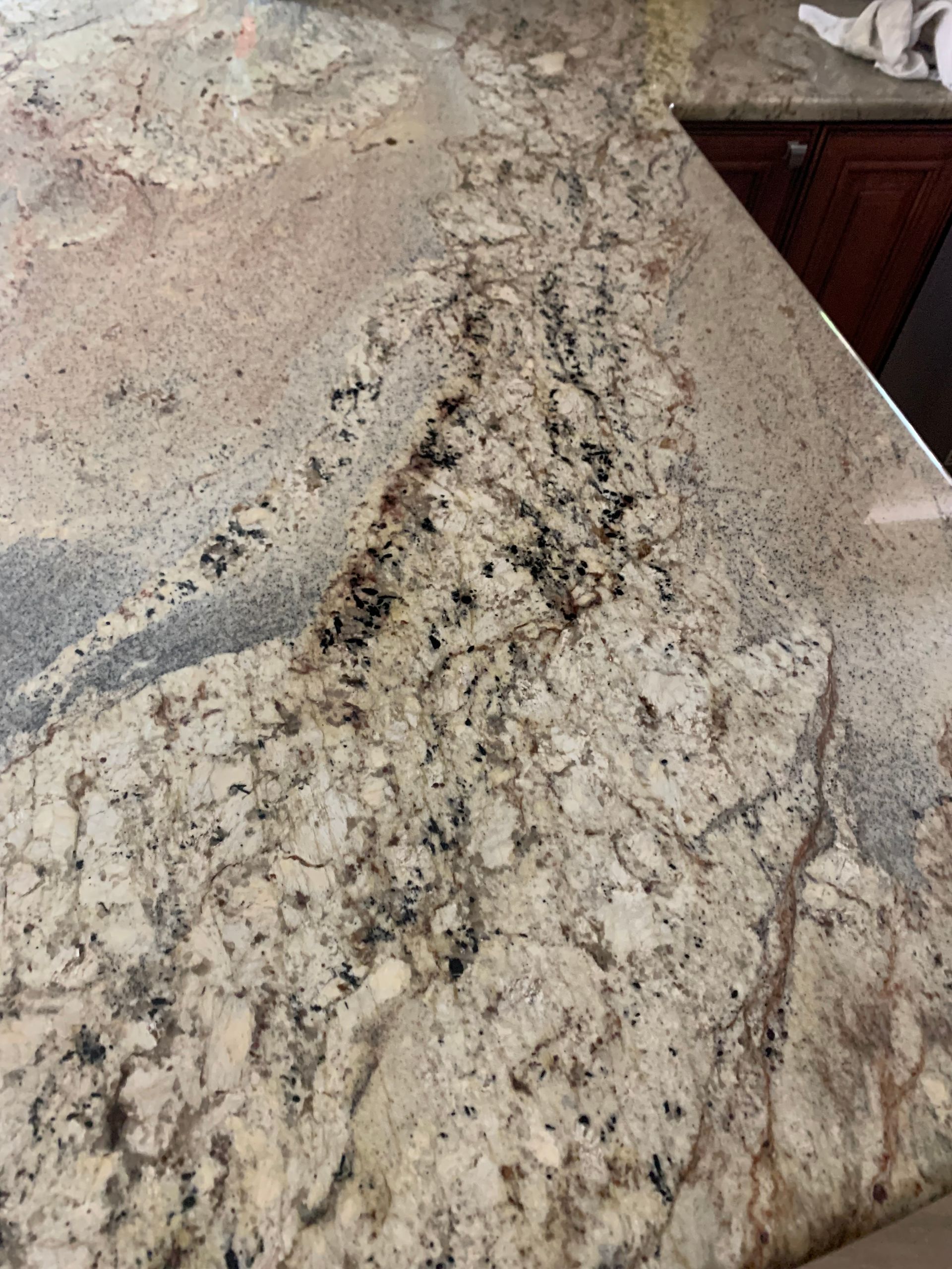 Close-up of a beige and gray speckled granite countertop with a dark wood cabinet edge.