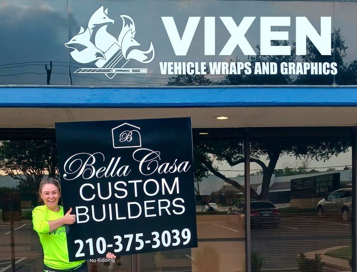 A woman holding a sign that says Bella Casa Custom Builders.