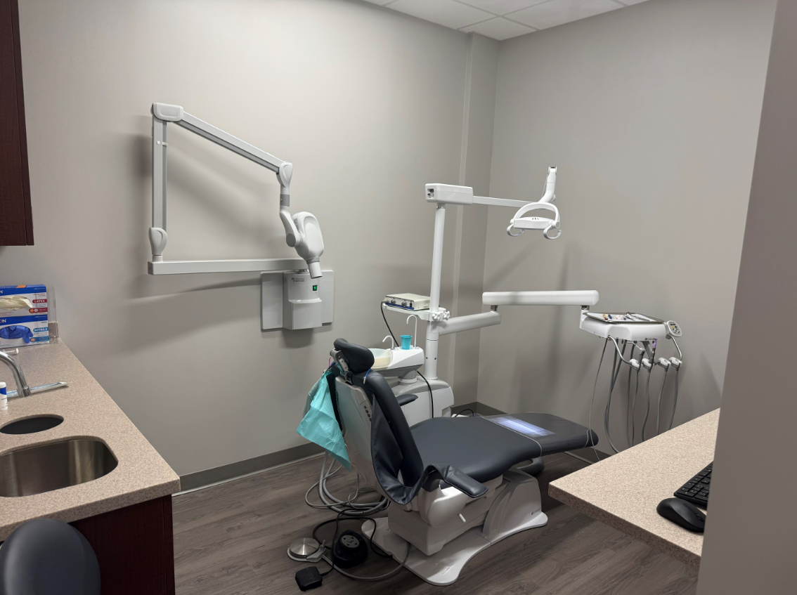 Dental exam room with chair, light, and equipment against gray walls.