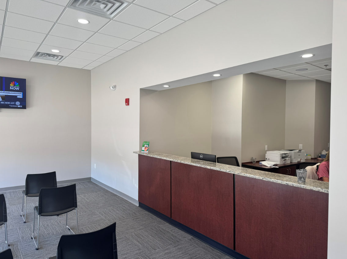 Reception area with a counter, chairs, and a television. Neutral-toned walls and flooring.