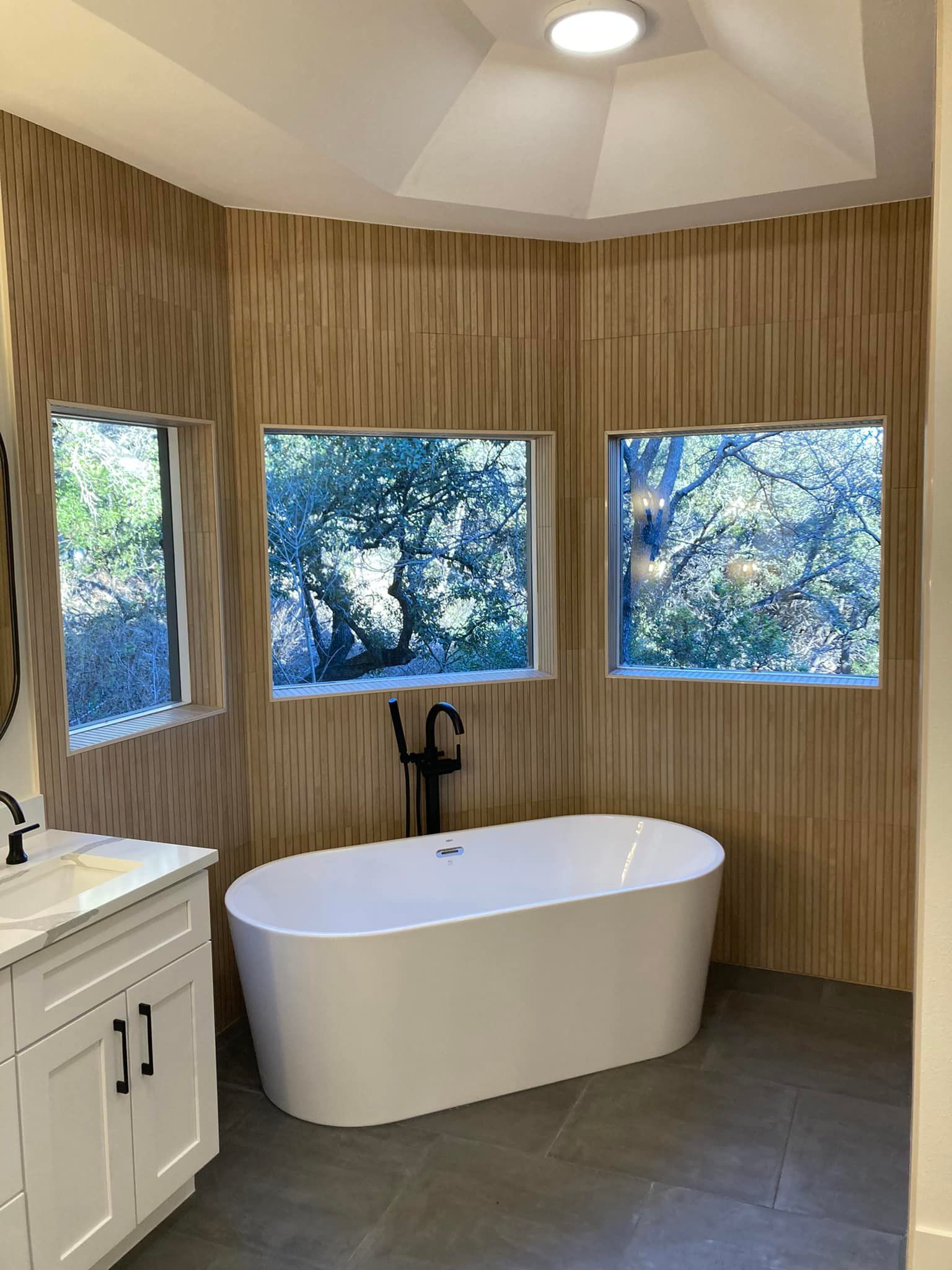A bathroom with a bathtub , sink , mirror and windows.