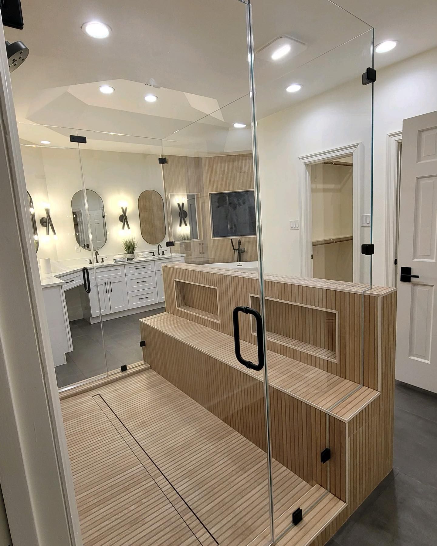 A bathroom with a wooden bench and a glass shower door.