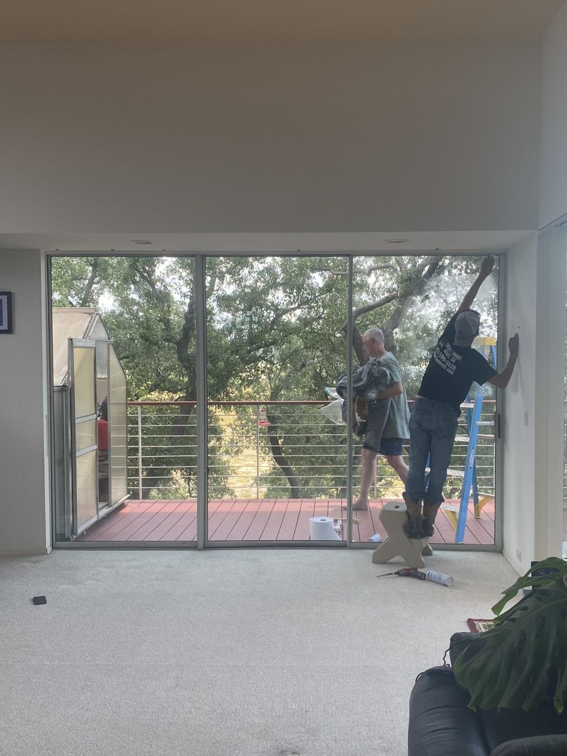 A man is standing on a ladder cleaning a window in a living room.