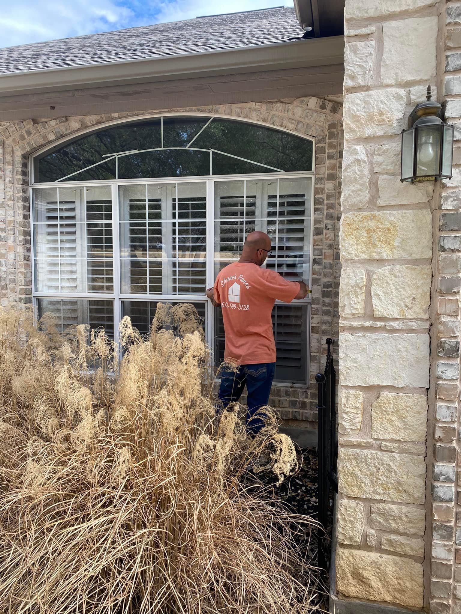 A man is cleaning a window in front of a brick house.