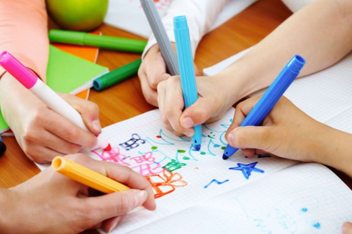 A group of children are drawing on a piece of paper with markers.