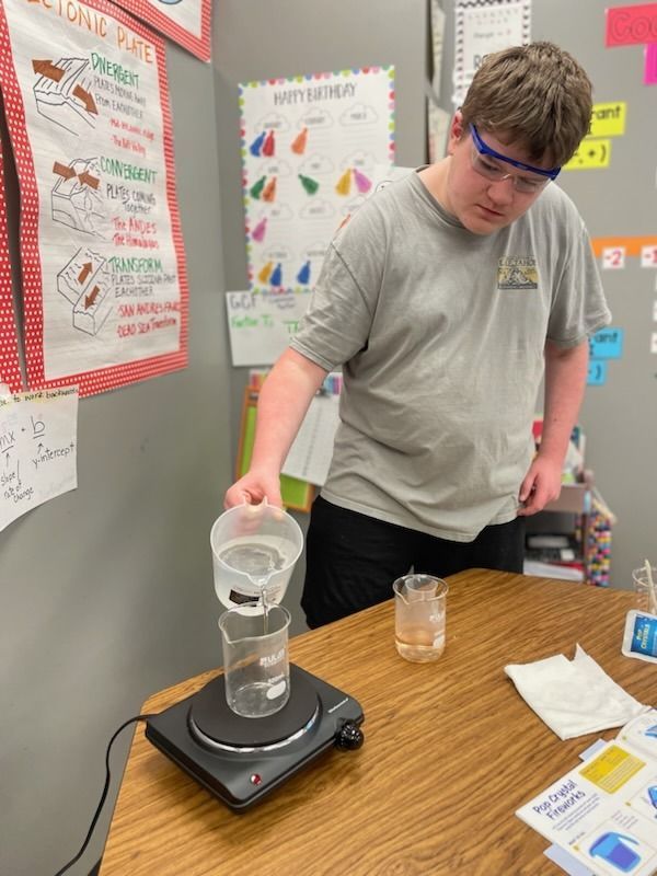 A boy is pouring water into a beaker on a stove.
