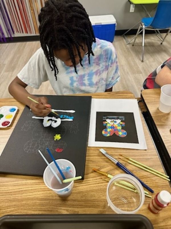 A young boy is sitting at a table painting a picture of a teddy bear.