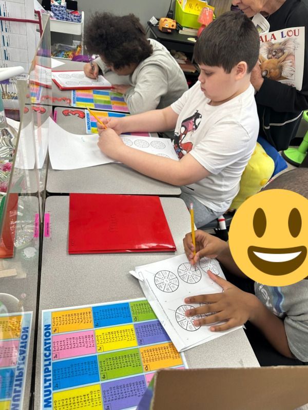 A group of children are sitting at a table with a poster that says multiplication on it