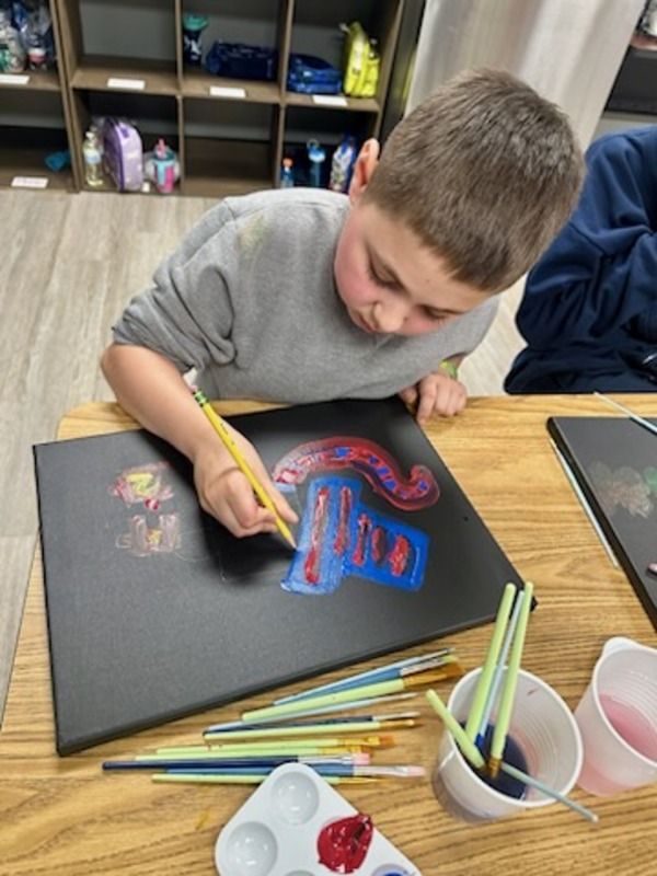 A young boy is sitting at a table painting on a canvas