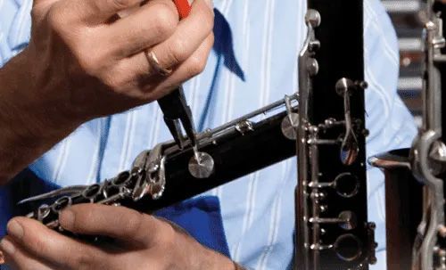 Person using pliers to adjust clarinet keys; close-up.