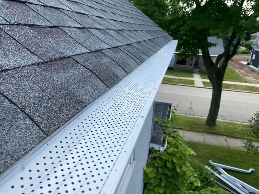 Gutter guard installed on a residential roof, protecting the gutter from debris, alongside street and tree.