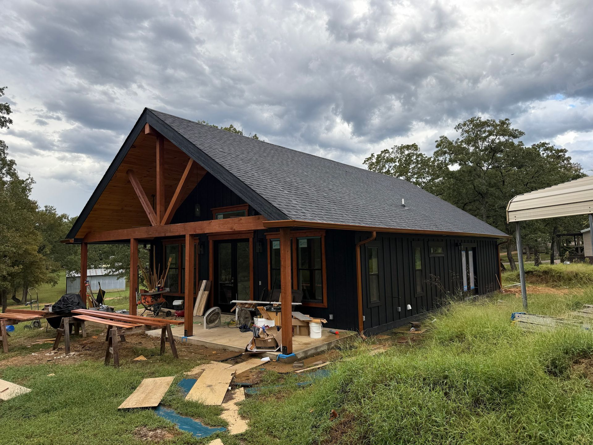 Black-sided house under construction with a wooden porch and a cloudy sky overhead.