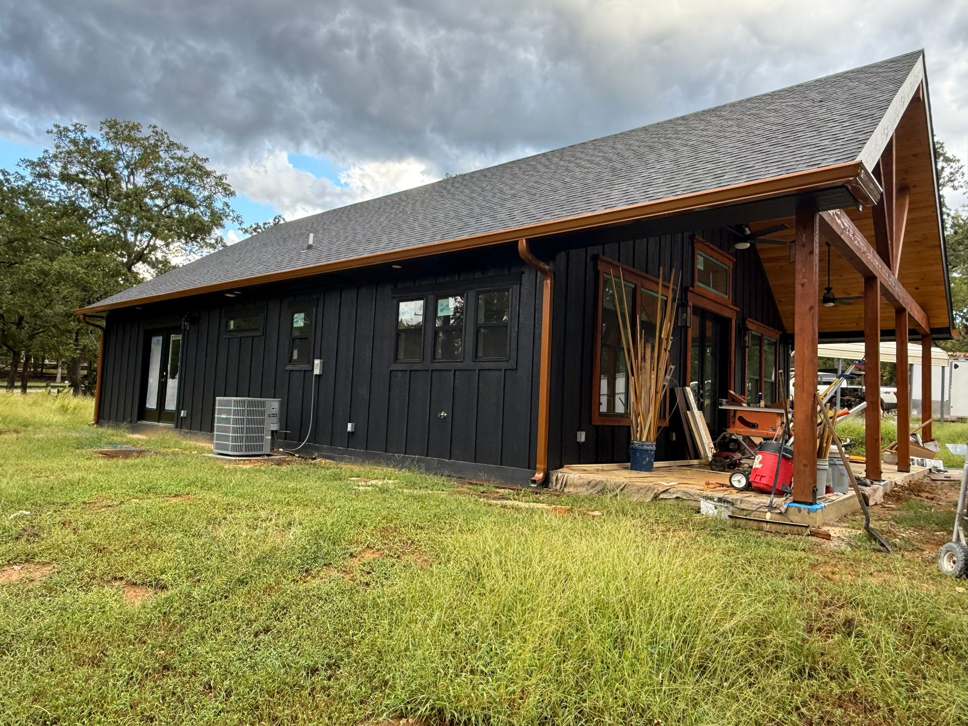 Black modern house with brown trim and dark roof, cloudy sky overhead.