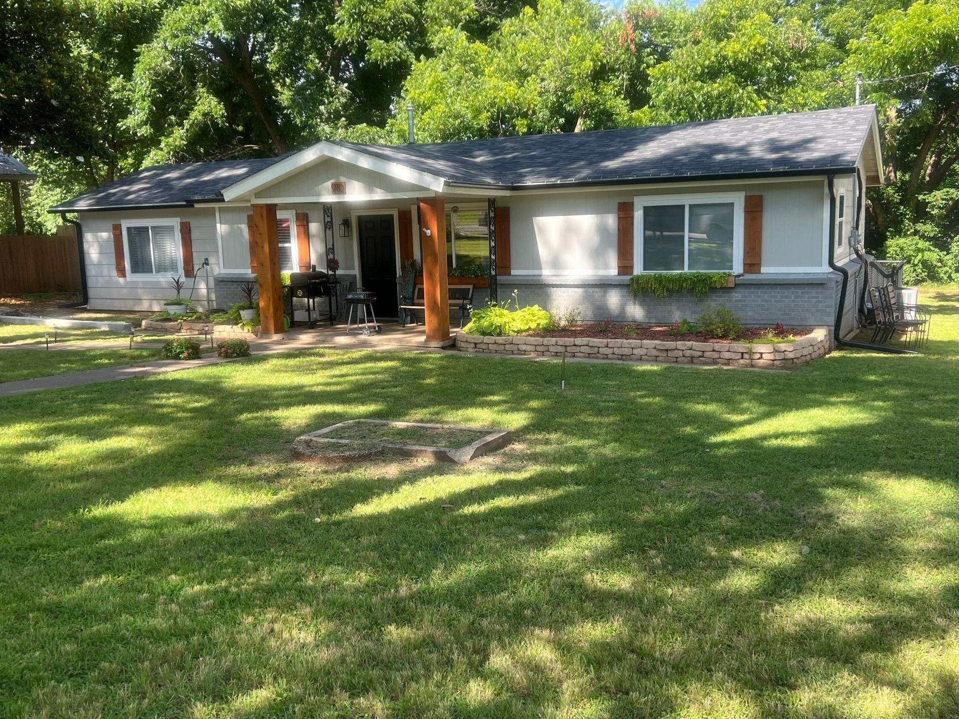 Ranch-style house with gray siding, brown shutters, and a covered porch with wooden posts, surrounded by a green lawn.