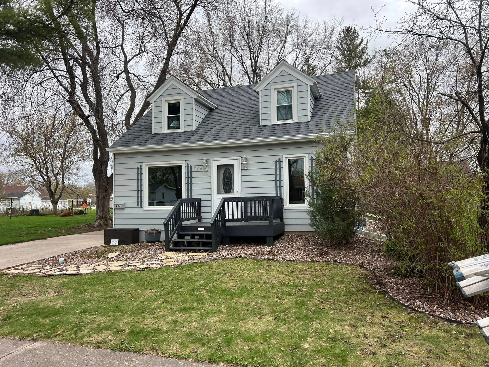 Small, light-blue house with gray roof, front steps, and two dormers; cloudy day.