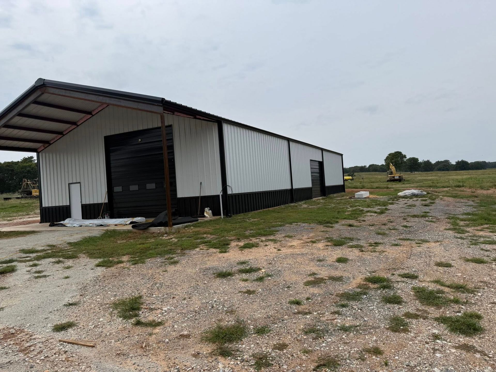 A large white and black metal building with an open garage door on a dirt lot.
