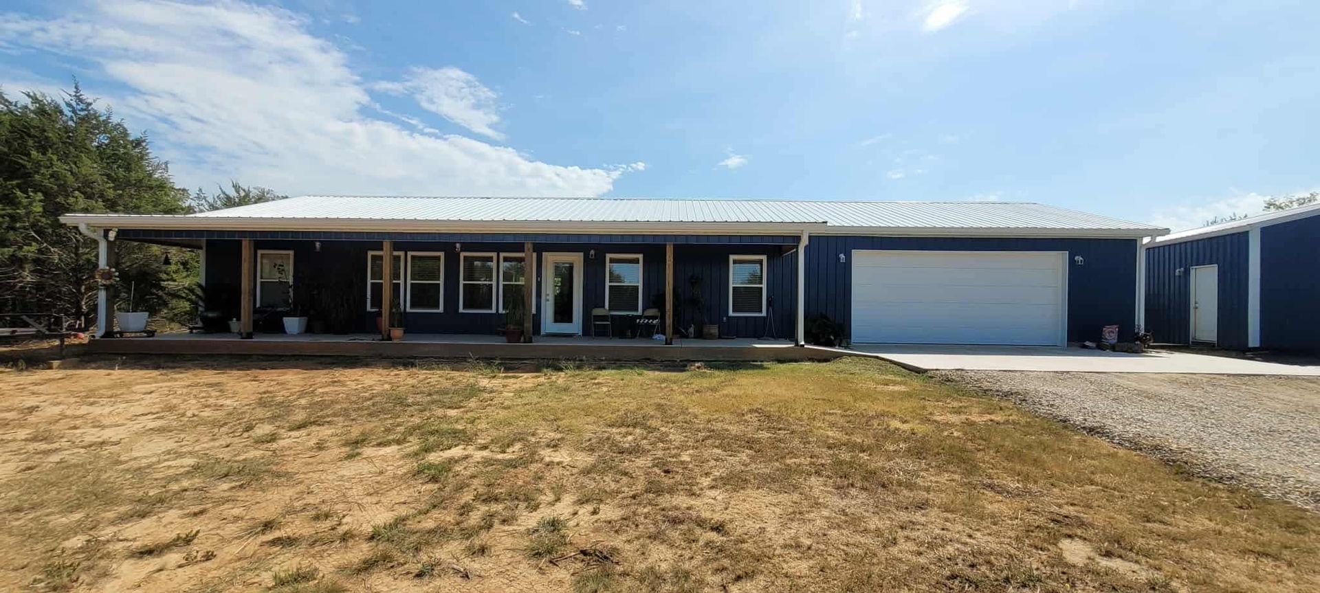 Blue house with white garage door and metal roof under a blue sky.