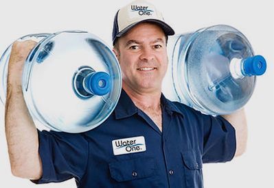 A man wearing a water one shirt is carrying two bottles of water