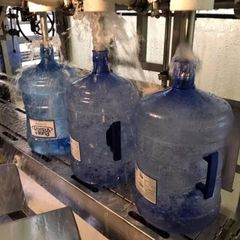 Three bottles of water are being poured into a machine.