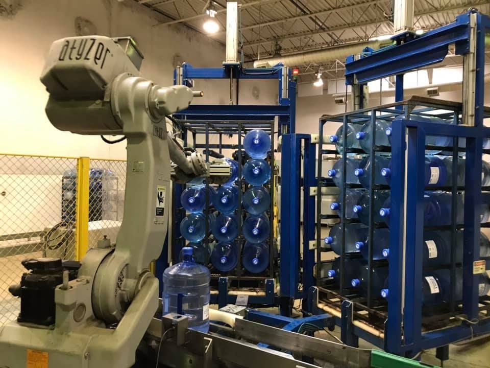 A robotic arm is moving water bottles on a conveyor belt in a factory.