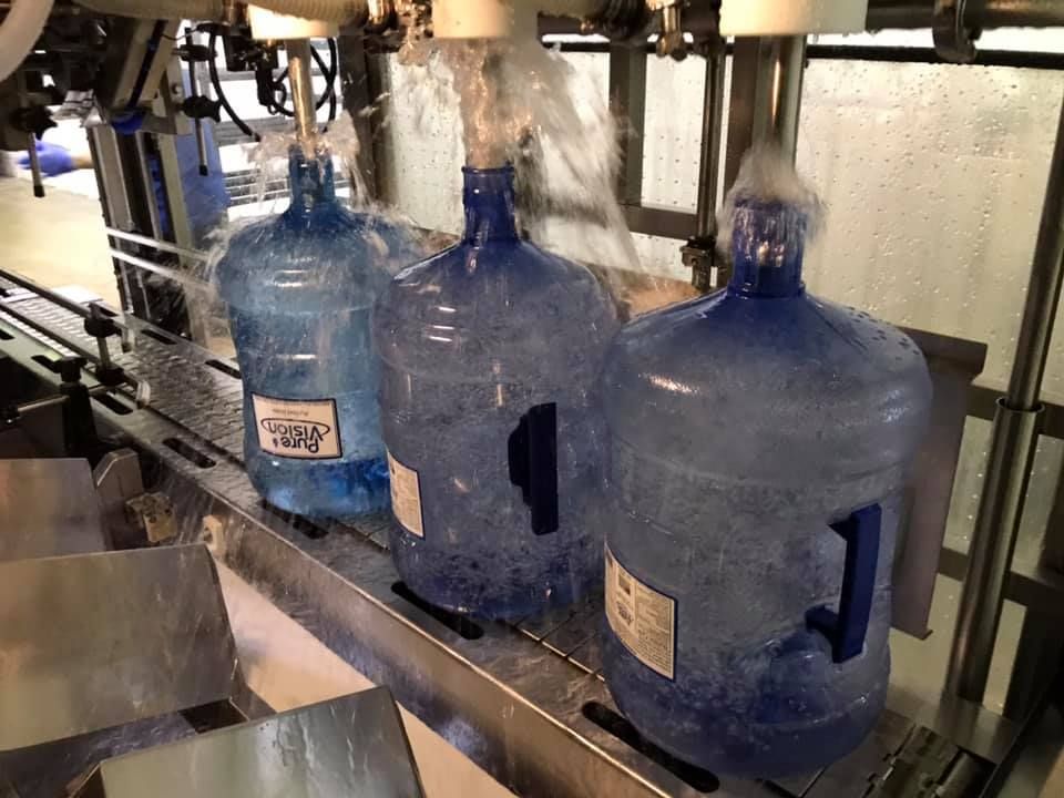Three bottles of water are being poured into a machine.