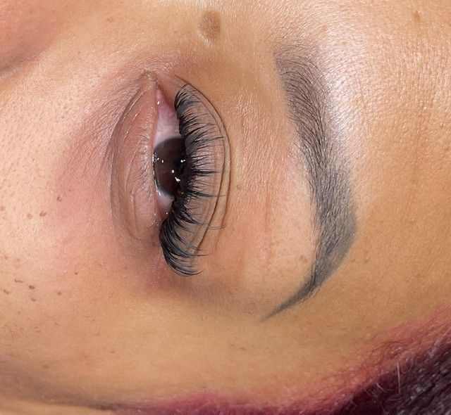 Close-up of a closed eye with long curled eyelashes and shaped eyebrow on a natural skin tone background