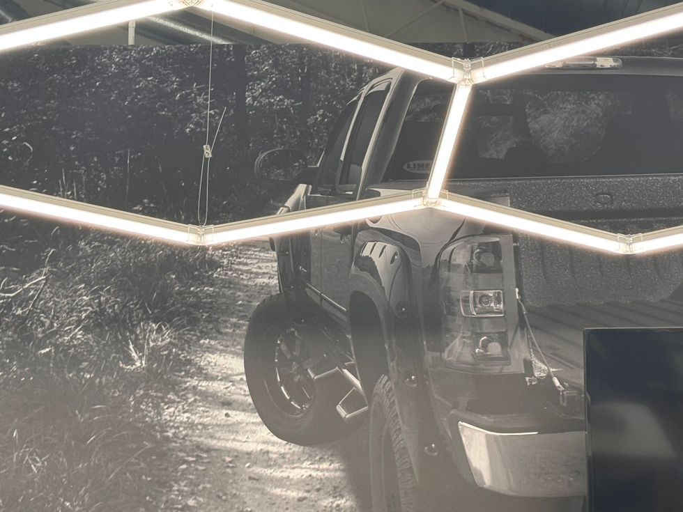 A pickup truck reflected in a glass surface at night, with bright geometric lights overhead.