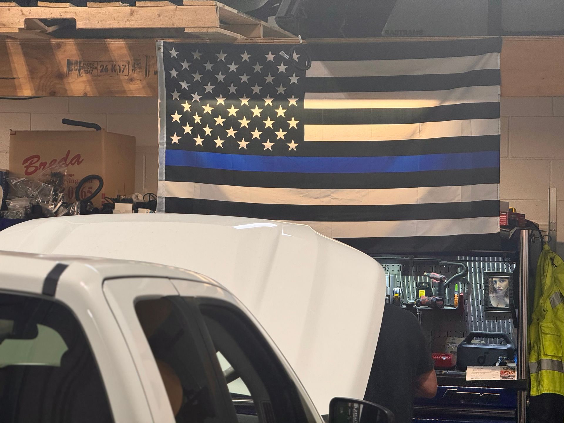 White pickup truck in a garage beneath a black-and-white American flag with one blue stripe