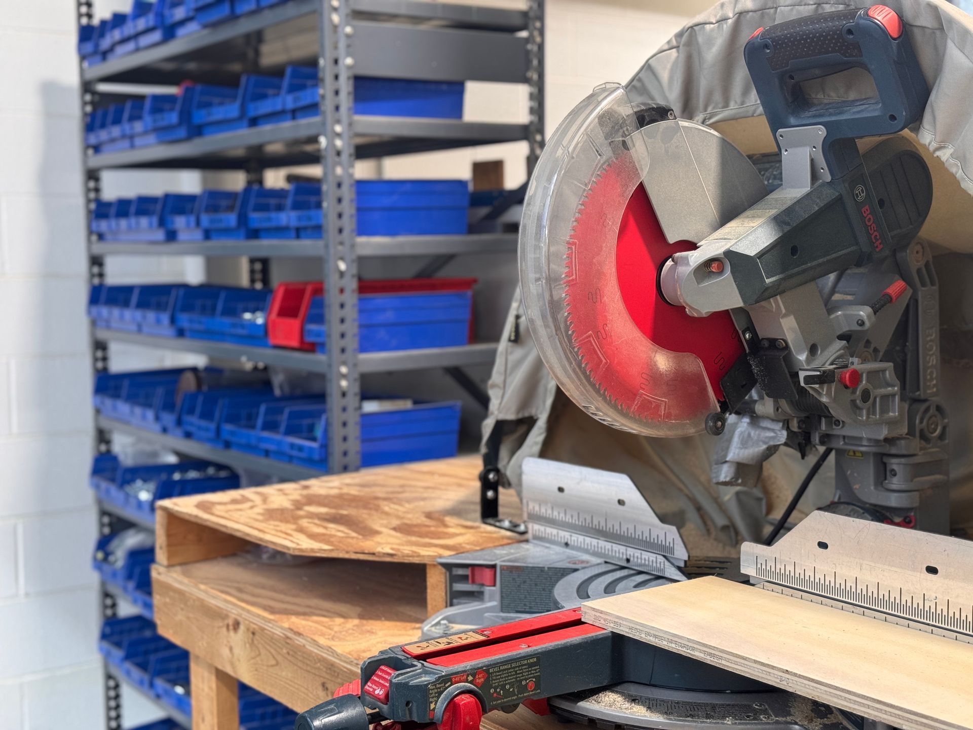 Miter saw on a workbench beside shelves of blue storage bins in a workshop