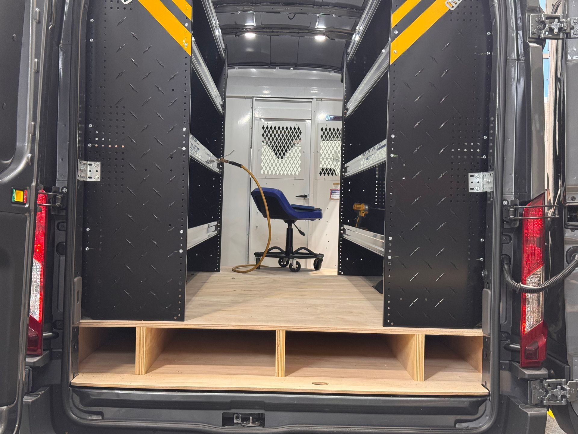 Cargo van interior with a small blue chair and wood flooring, viewed from the open rear doors.