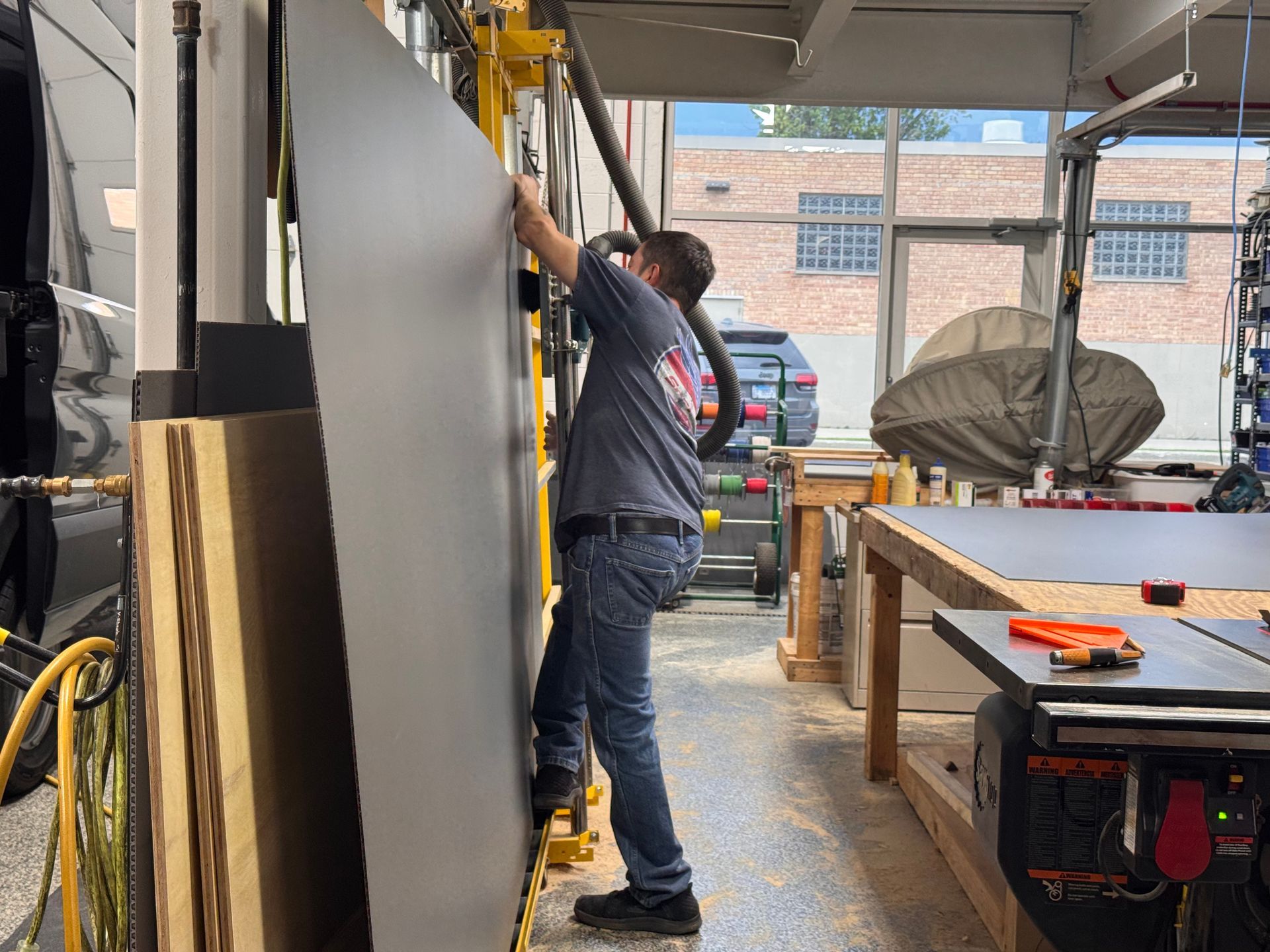 Person in blue overalls working on a wall in a workshop, with tools and tables nearby.