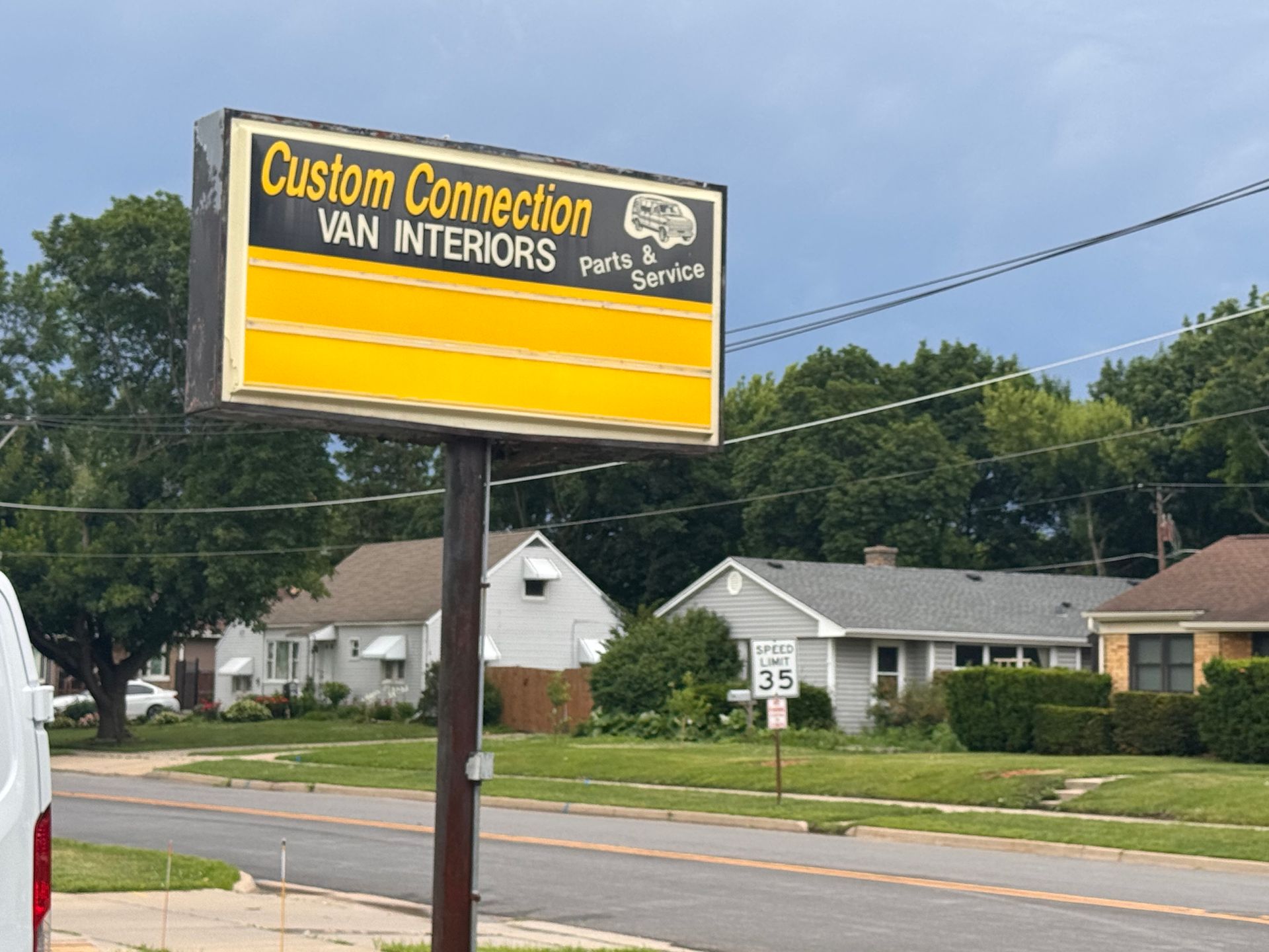 Yellow sign for “Custom Connection Van Interiors” beside a road in a suburban area