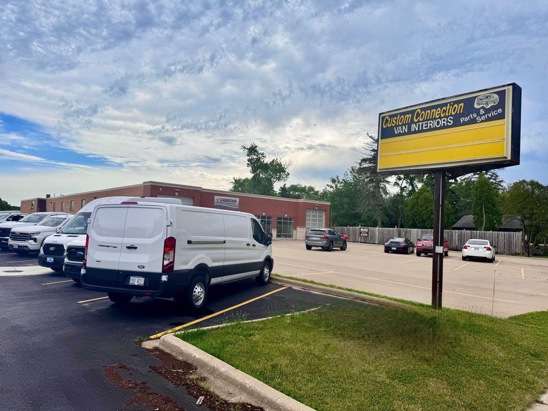 Parking lot with white vans beside a brick building and a large yellow roadside sign.