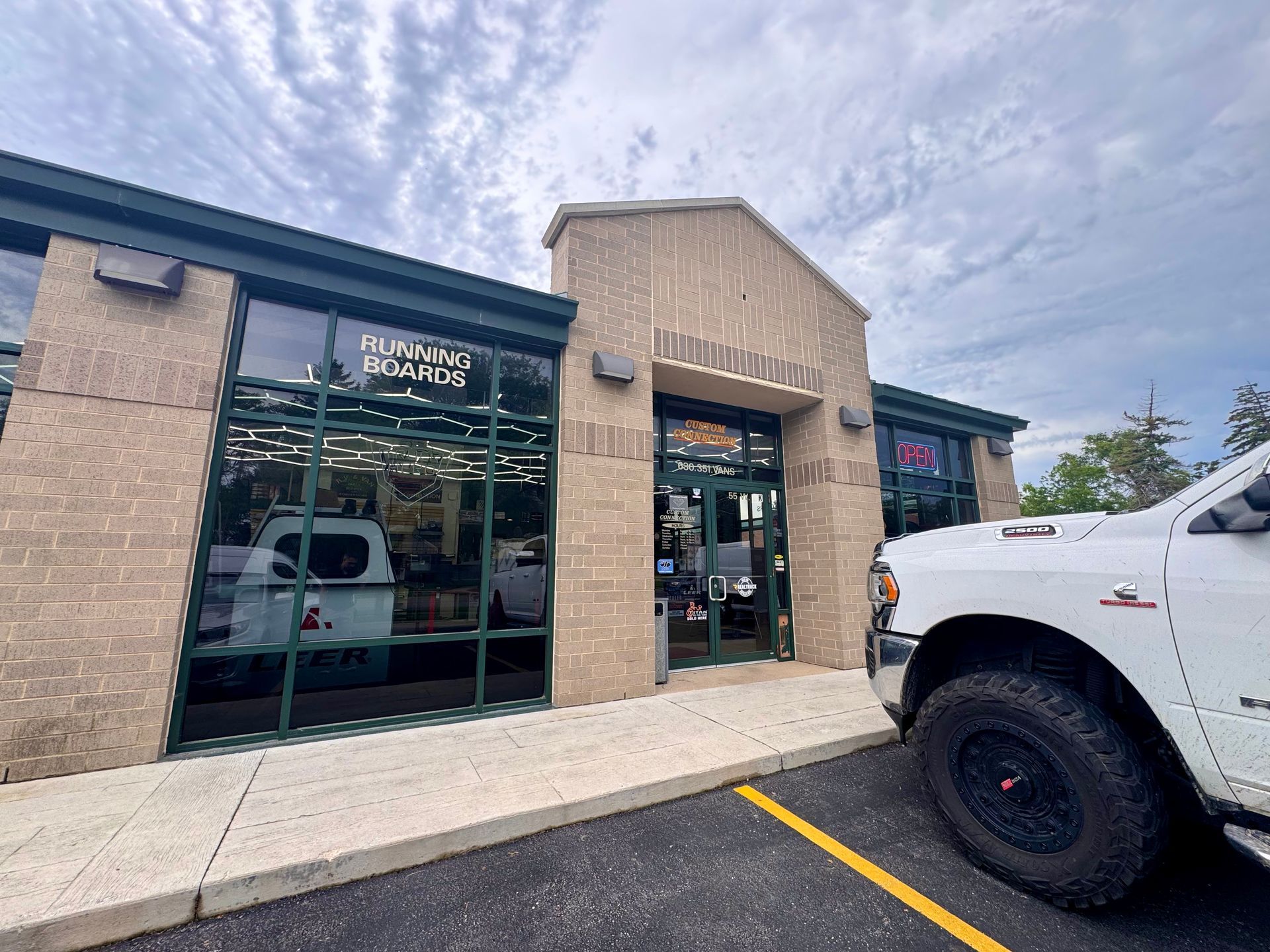 Strip-mall storefront with brick facade, glass windows, and a white truck parked outside