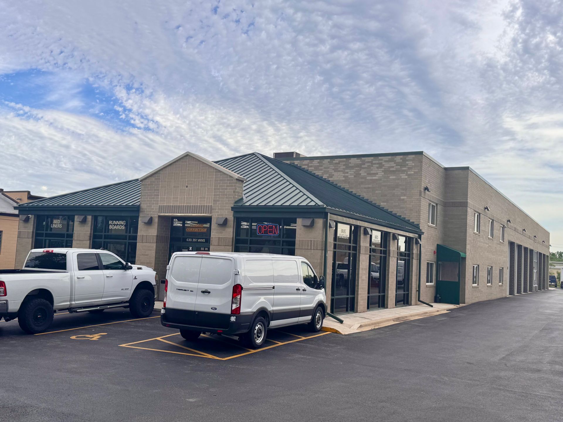 Strip mall storefronts with two white vans parked outside under a cloudy sky.