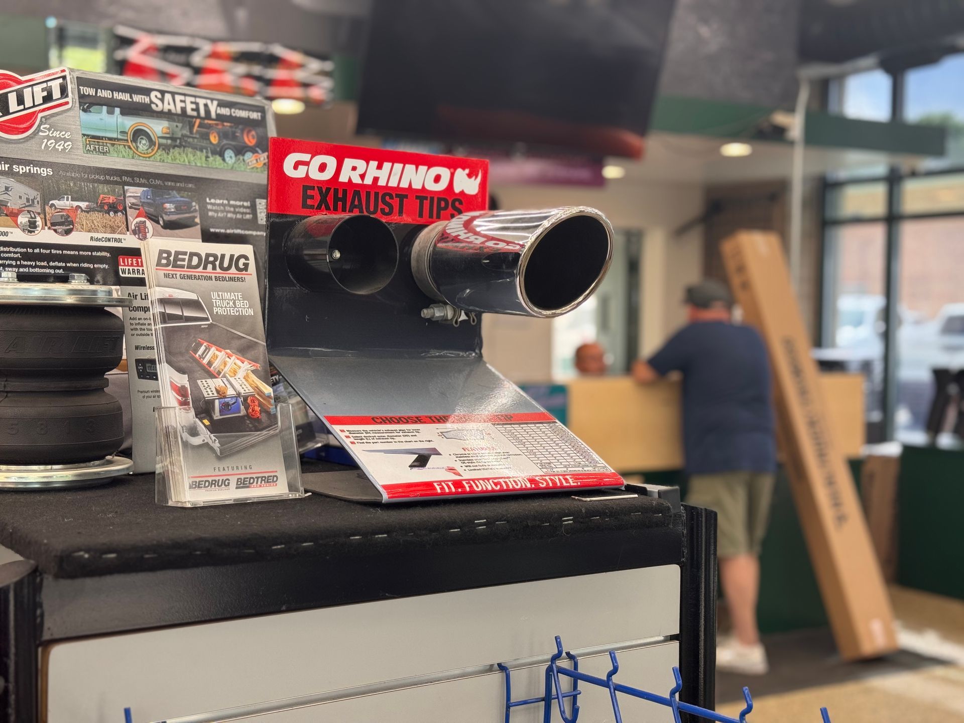 Red Rhino Exhaust Tips display on a counter in a shop, with a person browsing in the background.